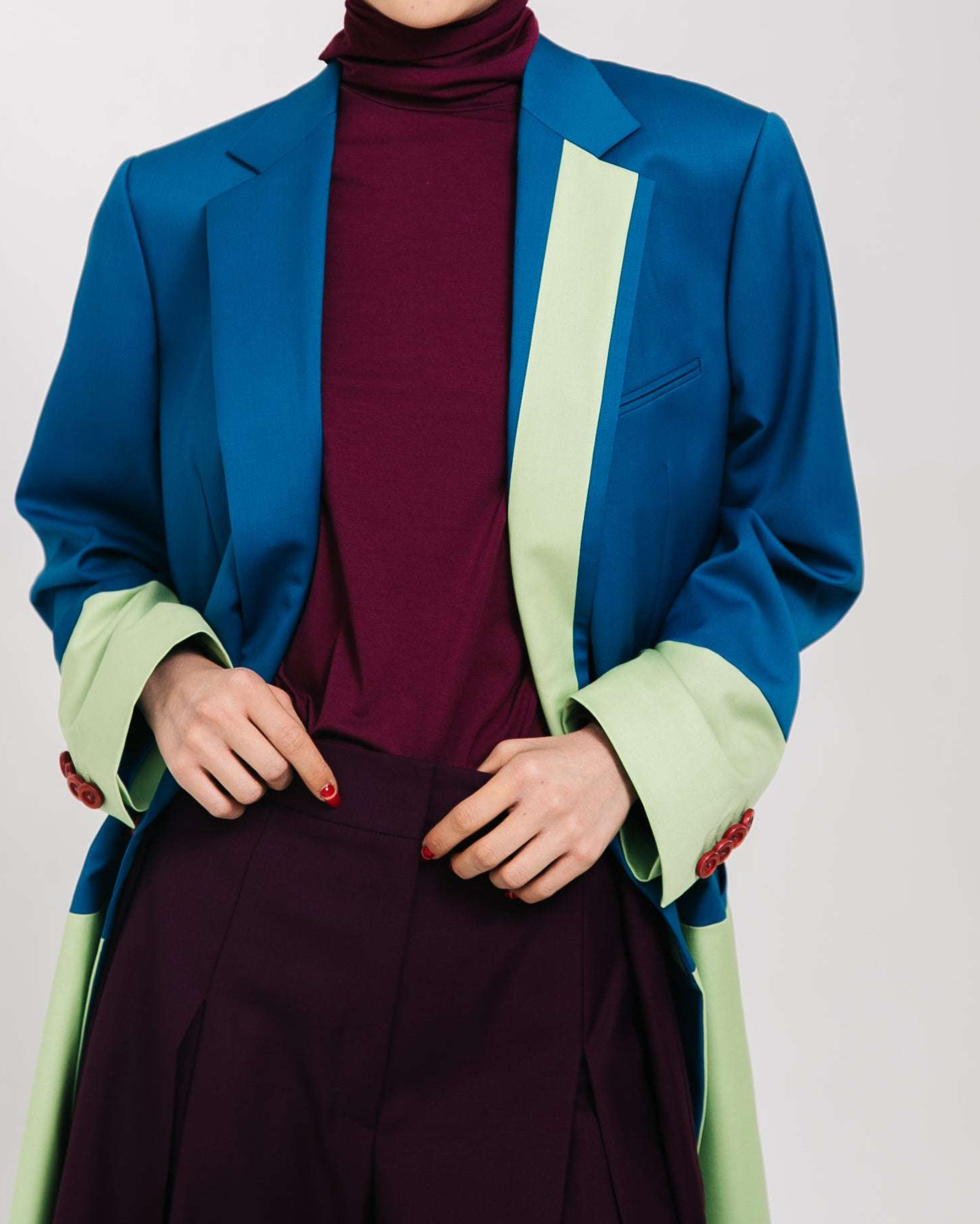 Two-Tone Wool Color Block Blazer featuring a vibrant cobalt blue base with soft pastel green accents on the cuffs and inner front panel, styled with rich burgundy turtleneck and high-waisted trousers for a sleek, gender-neutral suiting look.