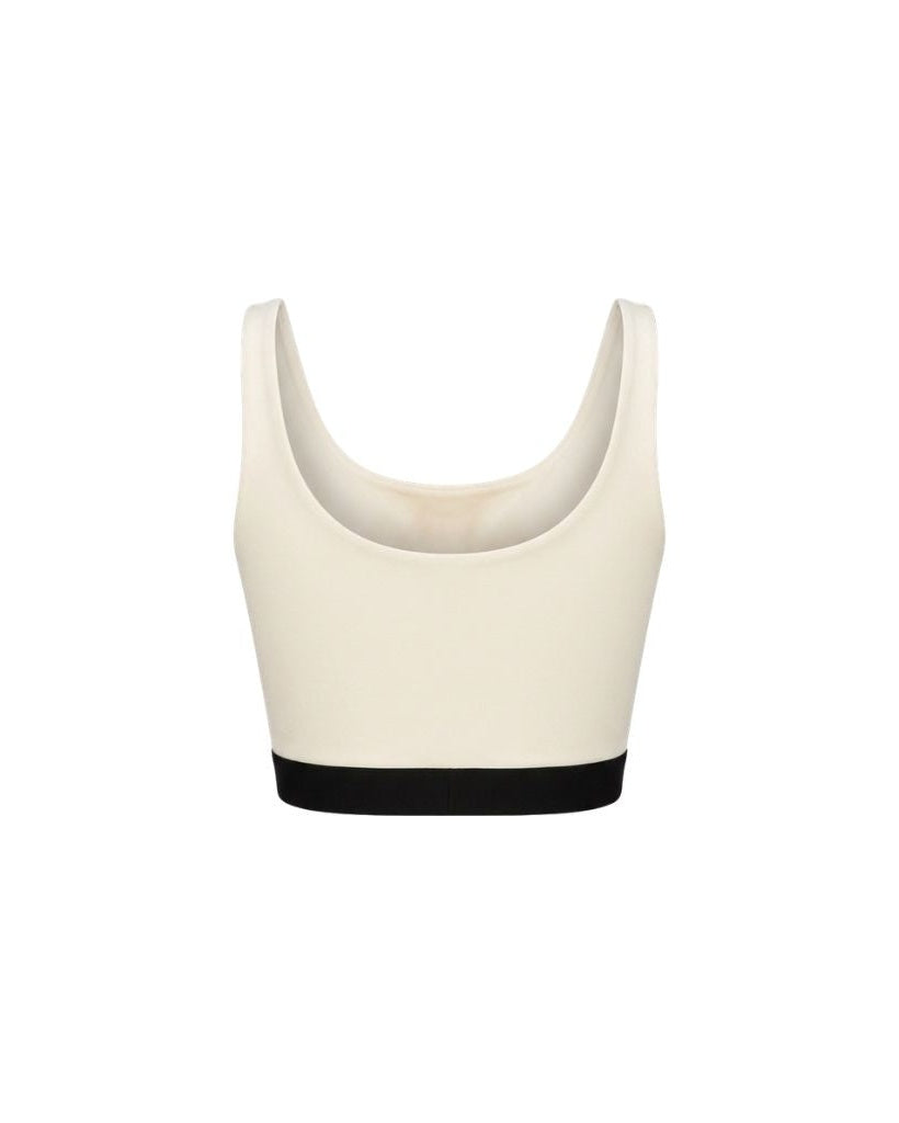 The Tailory New York X Dogpound Cropped Yoga Top in soft ivory with a scoop neckline and wide shoulder straps, finished with a contrasting black elastic band for support.