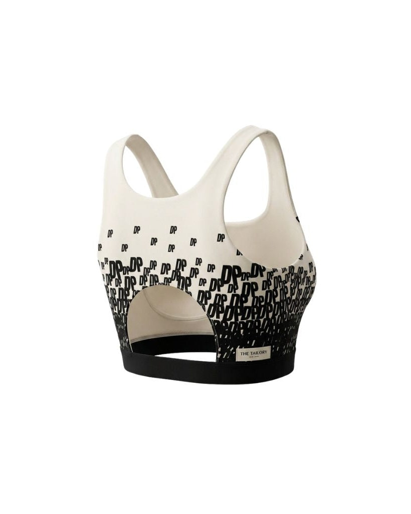 The Tailory New York X Dogpound Cropped Yoga Top in ivory with a black gradient "DP" logo pattern, featuring wide shoulder straps, a cut-out back detail, and a supportive black elastic hem band.