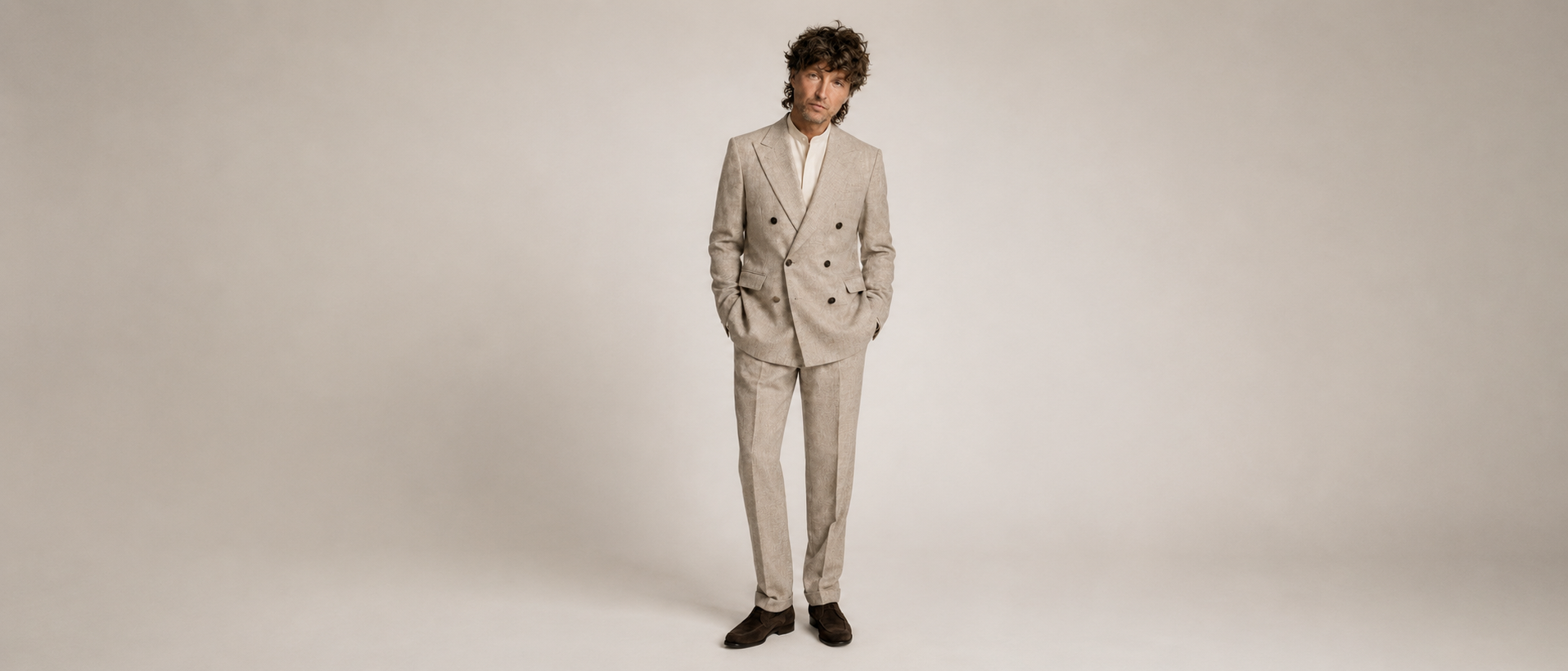 Man wearing a beige suit standing against a plain background