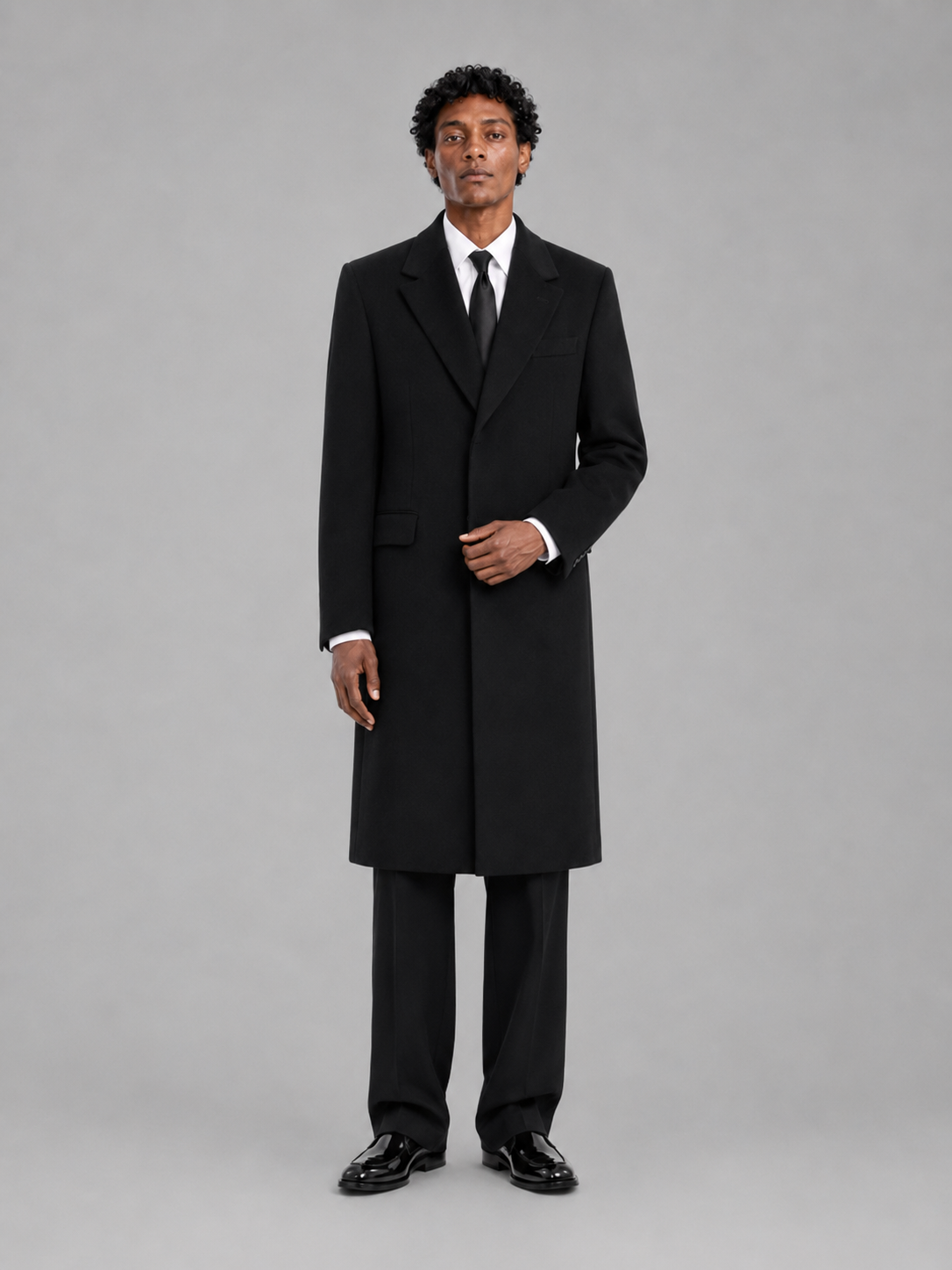 Man wearing a black overcoat and suit on a gray background
