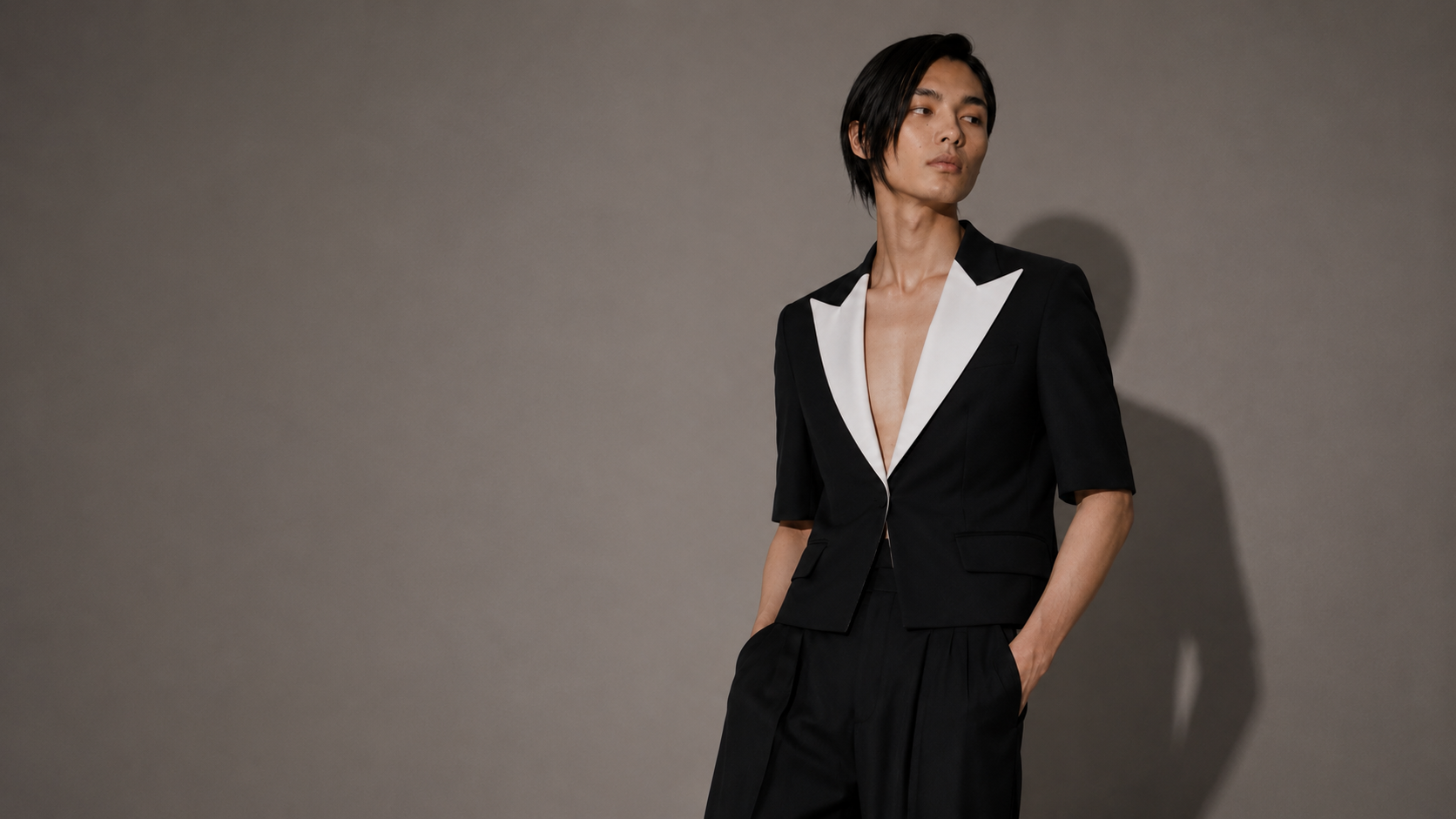 Person wearing a black suit with a white shirt against a gray background