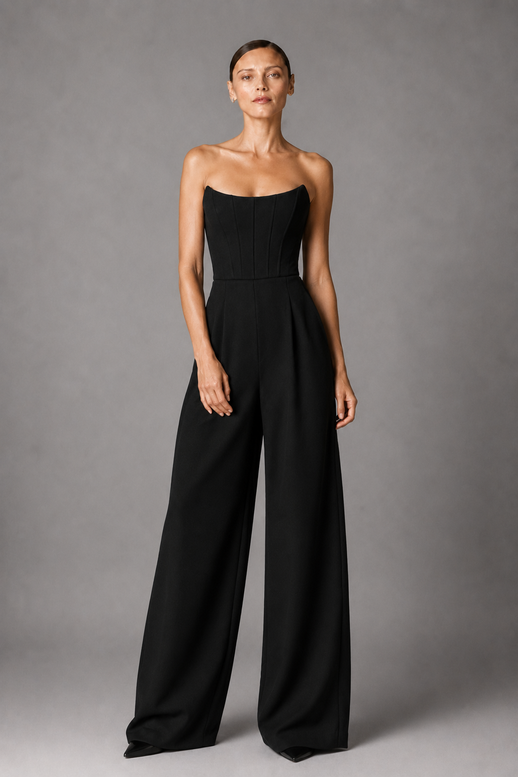 Woman wearing a black strapless corset jumpsuit against a gray background
