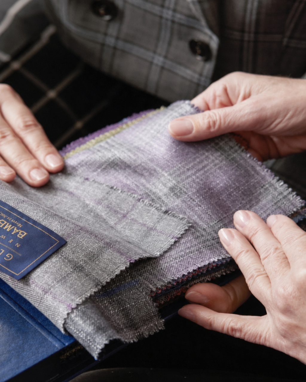 Hands selecting gray and lavender suit fabric swatches during a bespoke tailoring consultation at The Tailory New York.