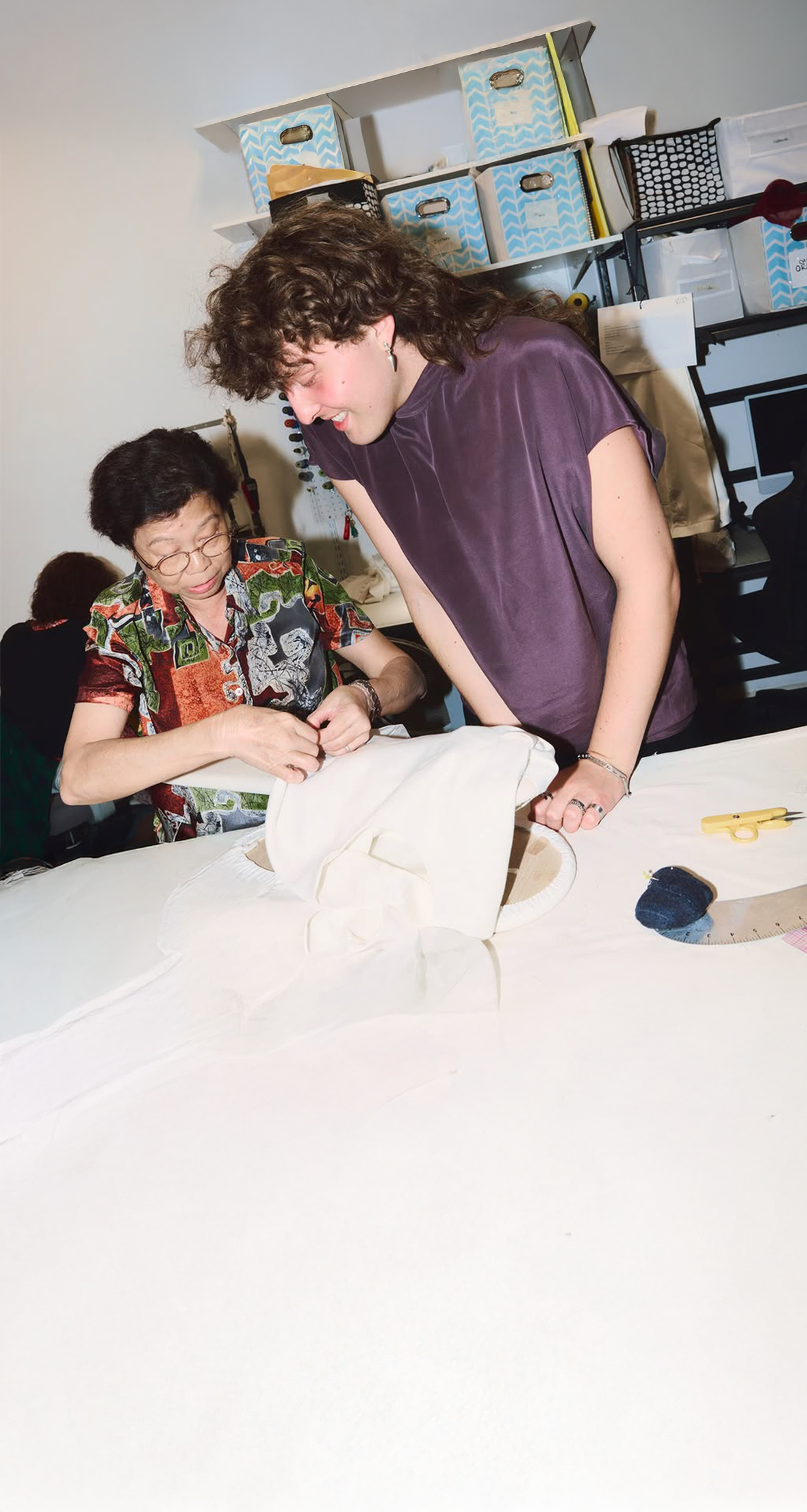 Two people working on a project at a table with various items in the background.