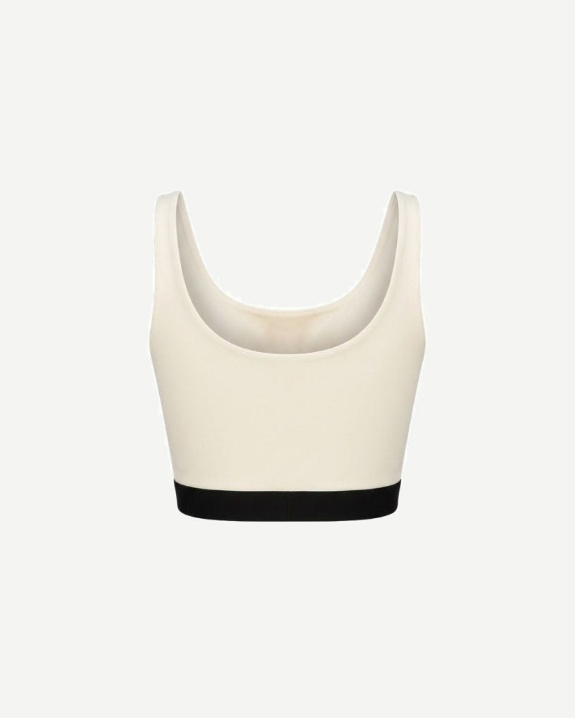 The Tailory New York X Dogpound Cropped Yoga Top in soft ivory with a scoop neckline and wide shoulder straps, finished with a contrasting black elastic band for support.